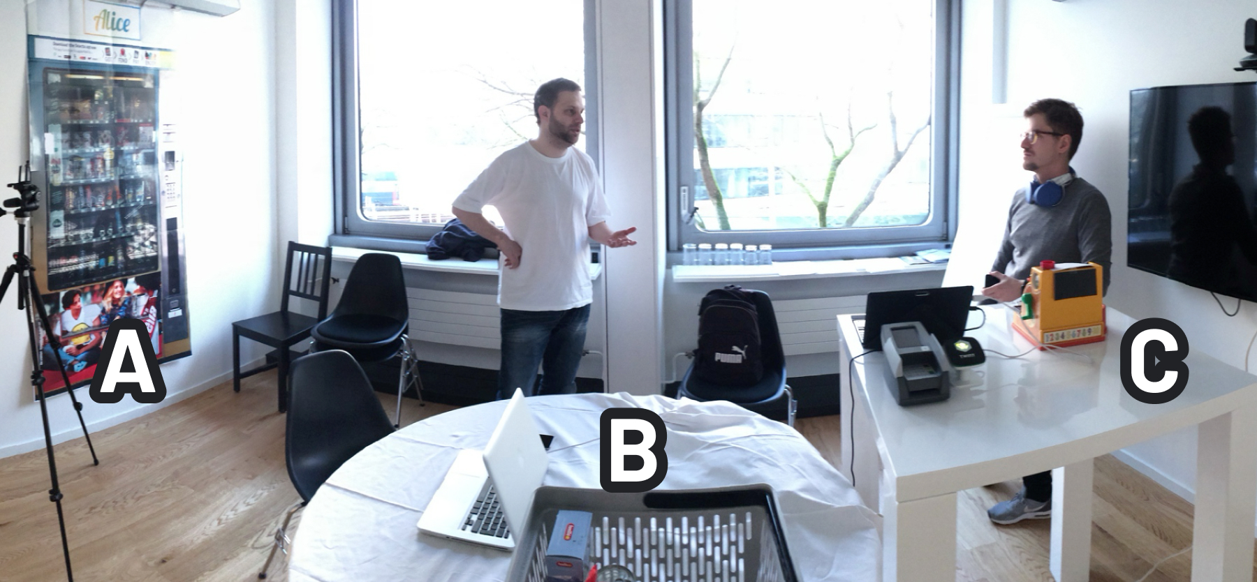 Lab setup for a Wizard-of-Oz user test with labeled stations: A shows a vending machine model, B a round table with laptop, and C the simulated checkout operated by a researcher.